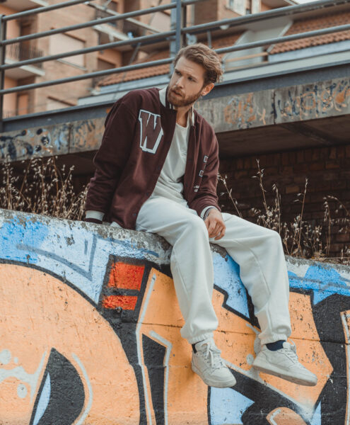 Modello seduto su un muretto con murales posa per foto moda di scarpe