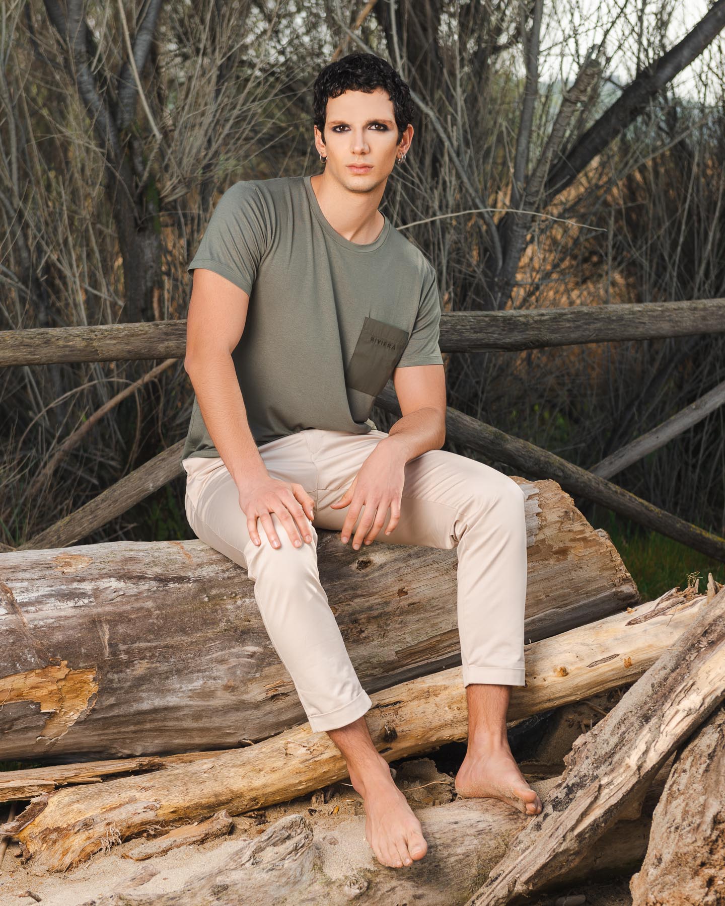 Modello seduto su un tronco in spiaggia per pubblicità abbigliamento da uomo