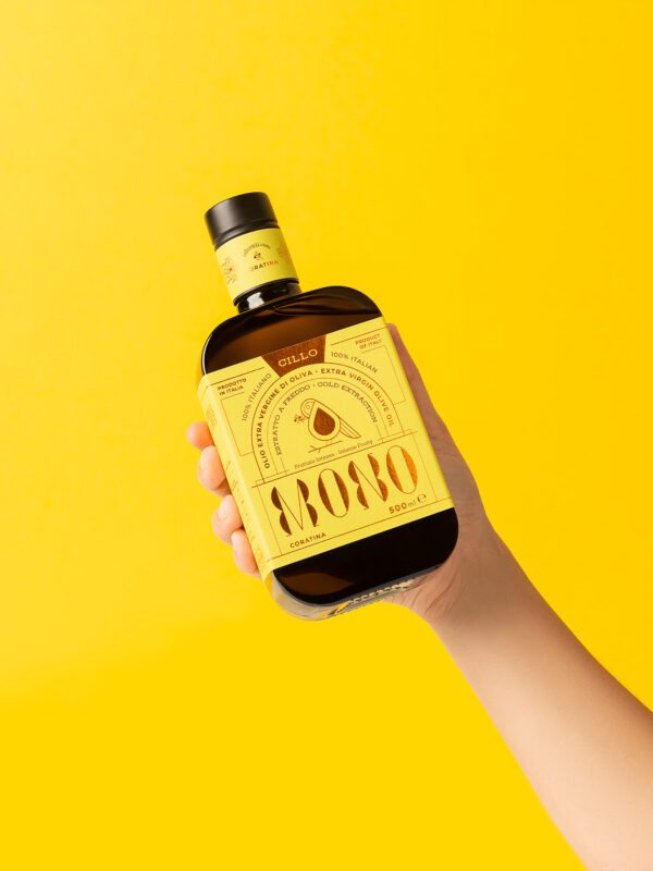 Still-life di prodotto per olio evo, mano di donna regge la bottiglia su sfondo giallo