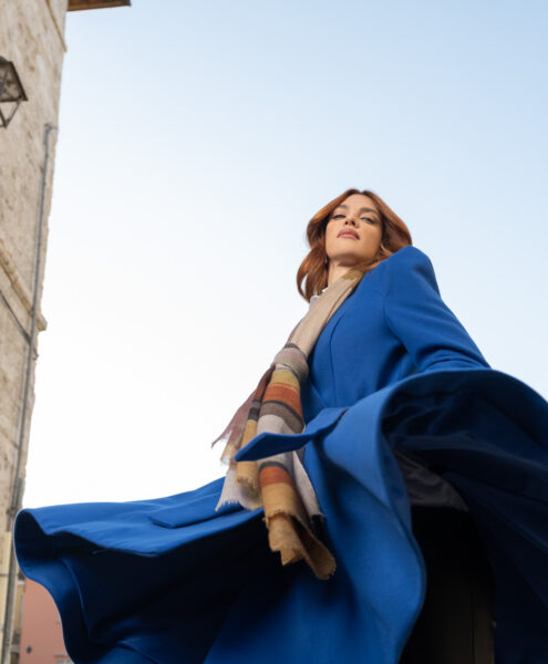 Modella con cappotto blu e sciarpa, posa per un servizio di moda ad Ascoli Piceno